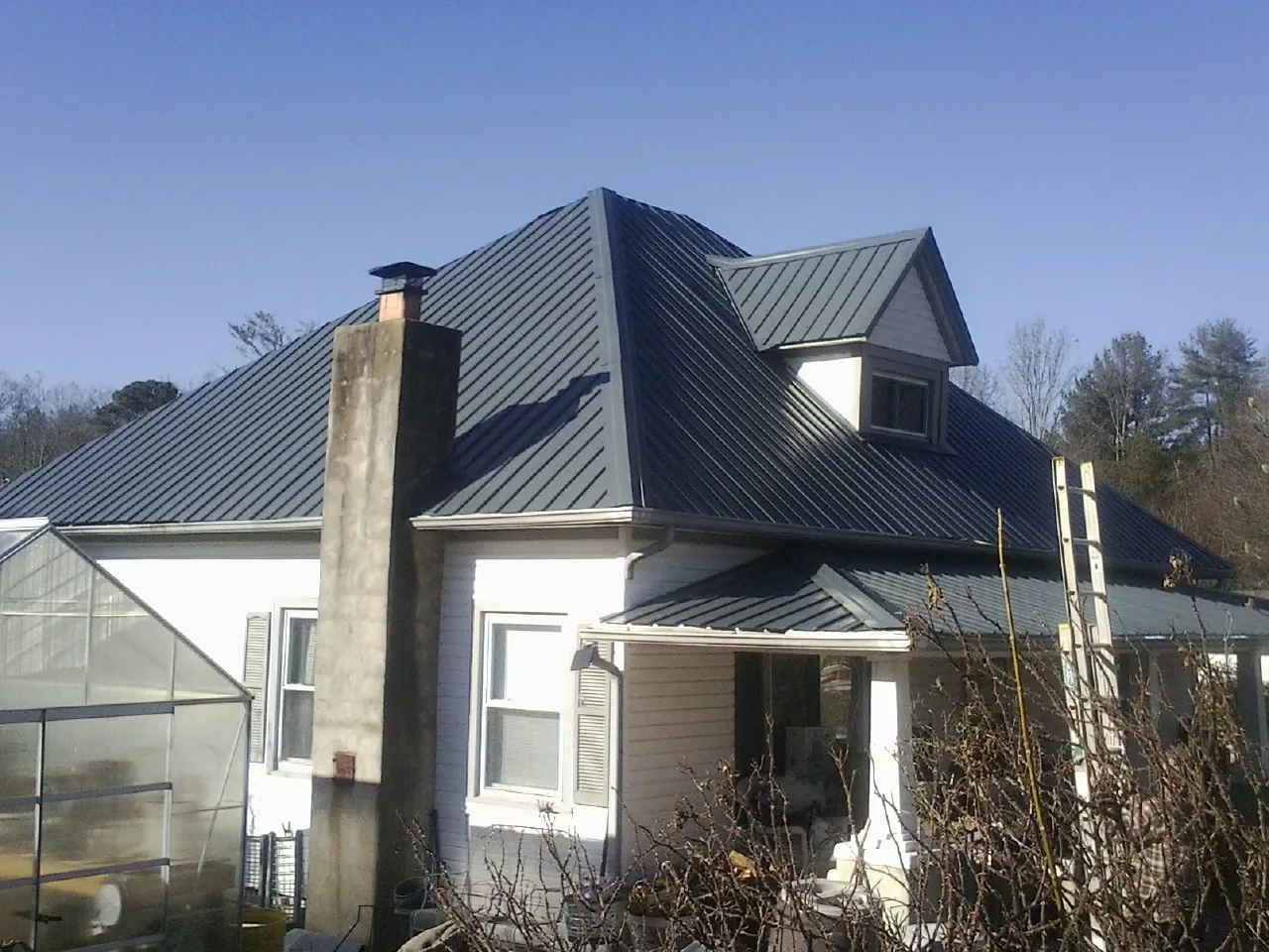 Dark blue standing seam metal roof on a white farmhouse with dormer — Slate & Tile Roof Repair by Roofing Brothers in Laurens