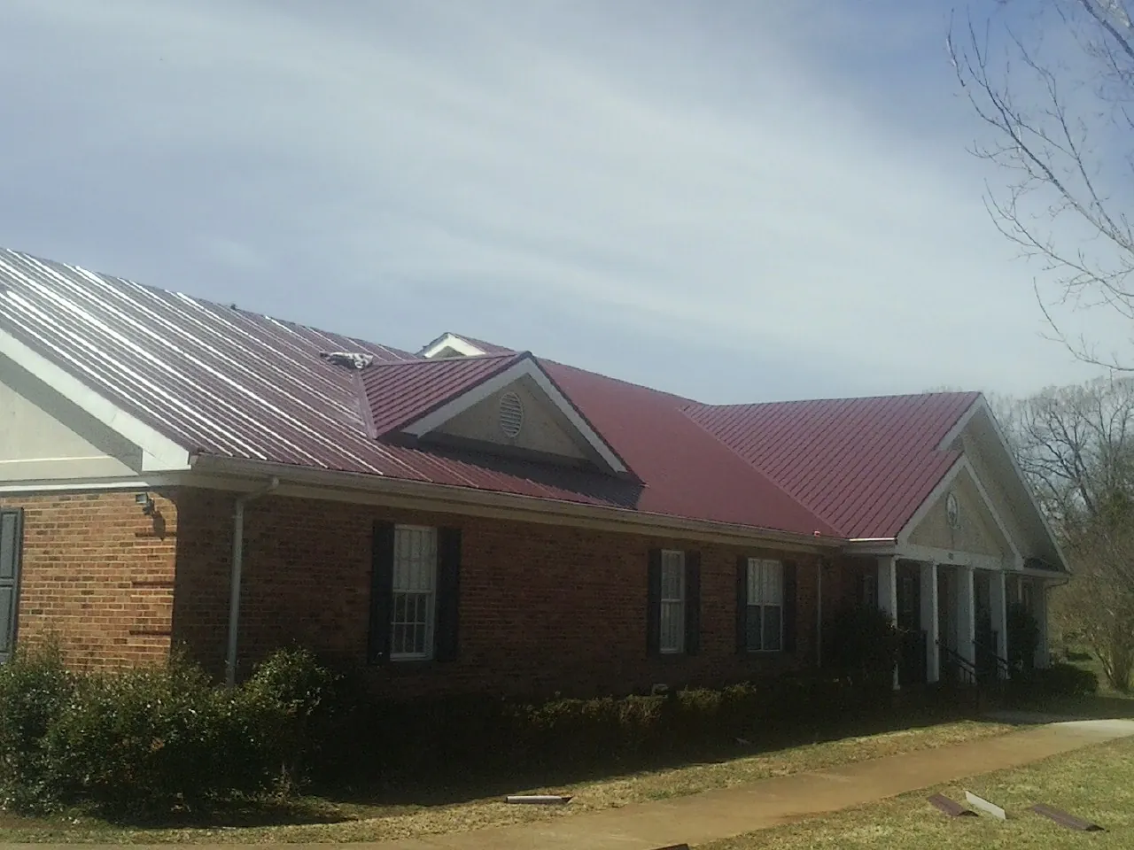 Red metal roof with gabled entries on a long brick building, from a Hail Damage Roof Repair job in Laurens